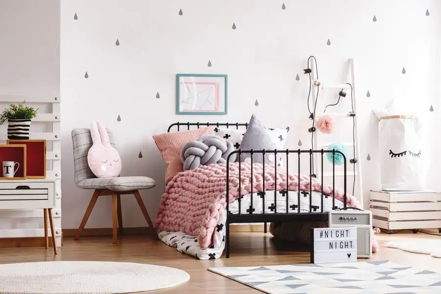 Charming children's bedroom with a black metal bed, pink and gray bedding, playful decor, and a bunny pillow.