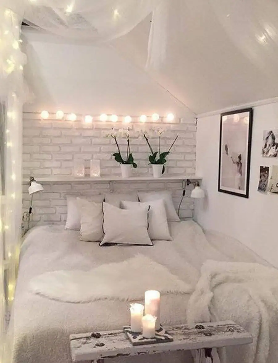 Cozy attic bedroom with white brick walls, soft bedding, fairy lights, and minimalistic decor.