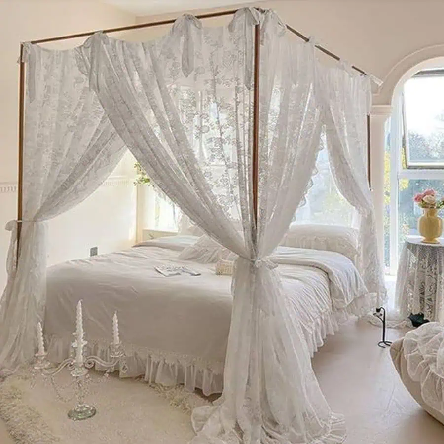 Canopy bed with white lace curtains, light-filled room, flowers on a side table, romantic decor.