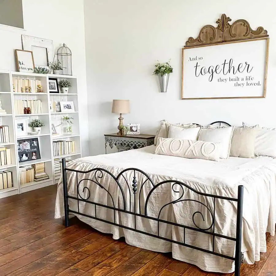 Farmhouse-style bedroom with a black metal bed frame, cozy neutral bedding, and a decorative sign above the bed.