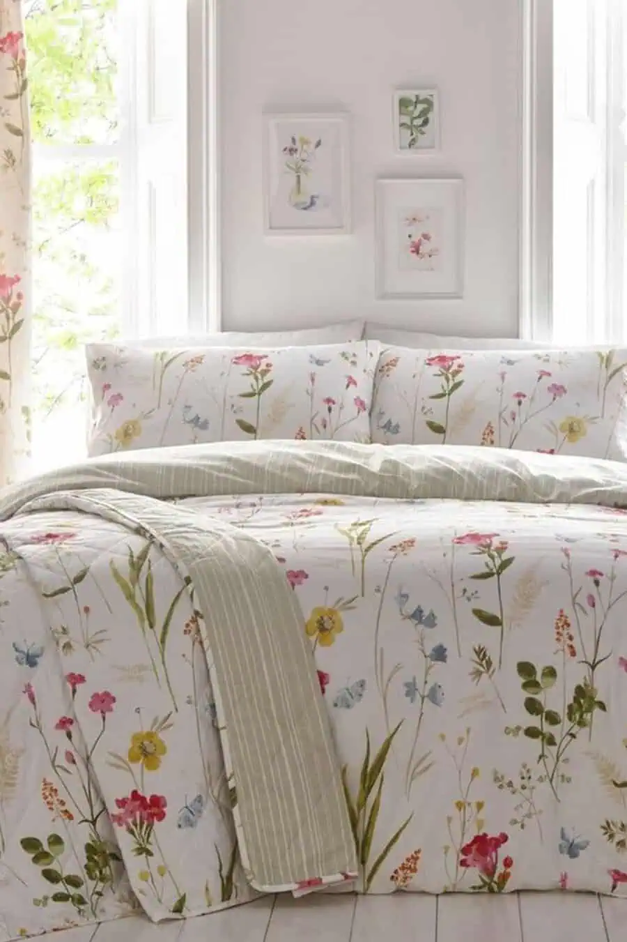 A bed with floral-patterned bedding and green striped throw blanket in a bright room with framed art.