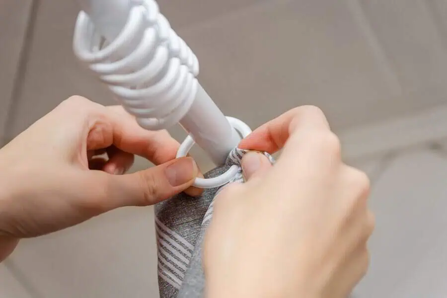 Hands attaching a curtain with white rings to a rod