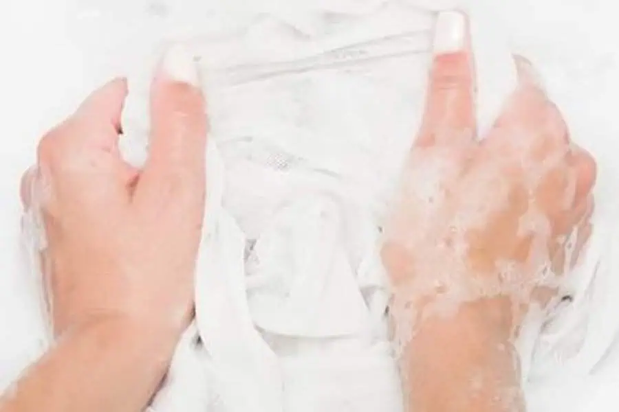 Hands washing a white garment with soap suds