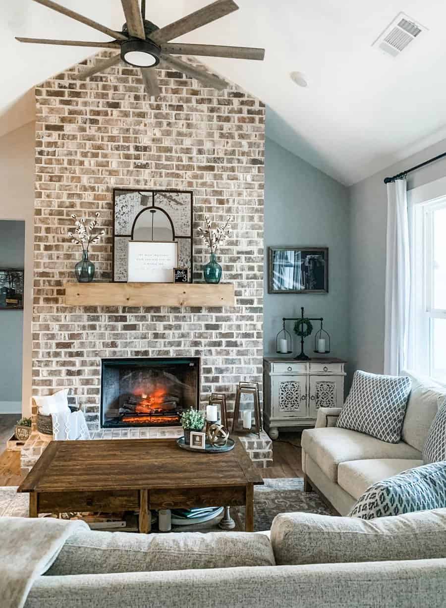 Above fireplace decor with rustic brick accent wall, wooden mantel, framed art, and teal vases.