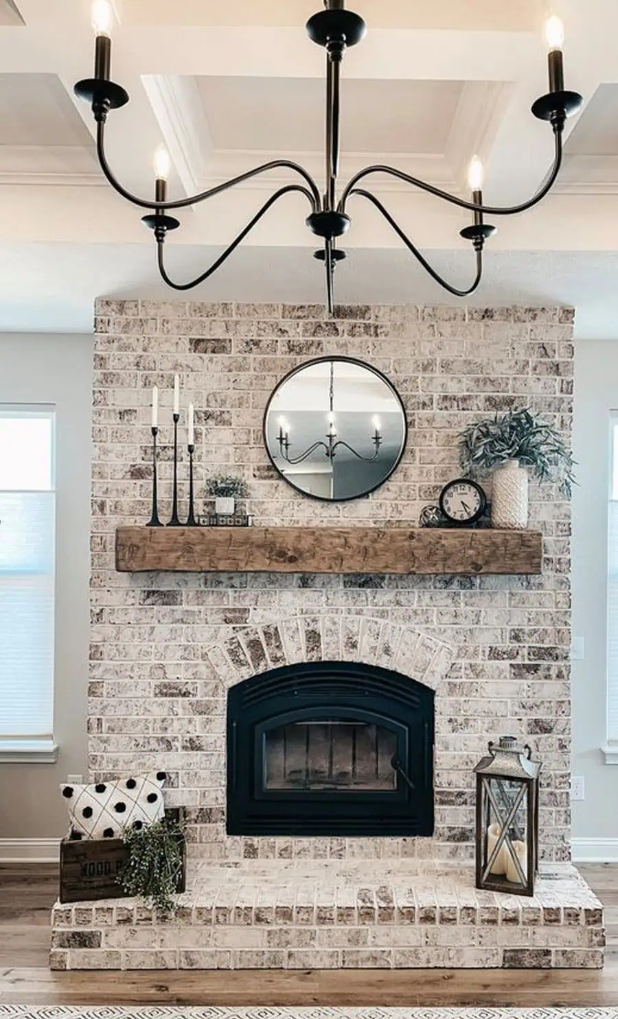 Above fireplace decor featuring rustic brick, wooden mantel, round mirror, candles, and lantern.