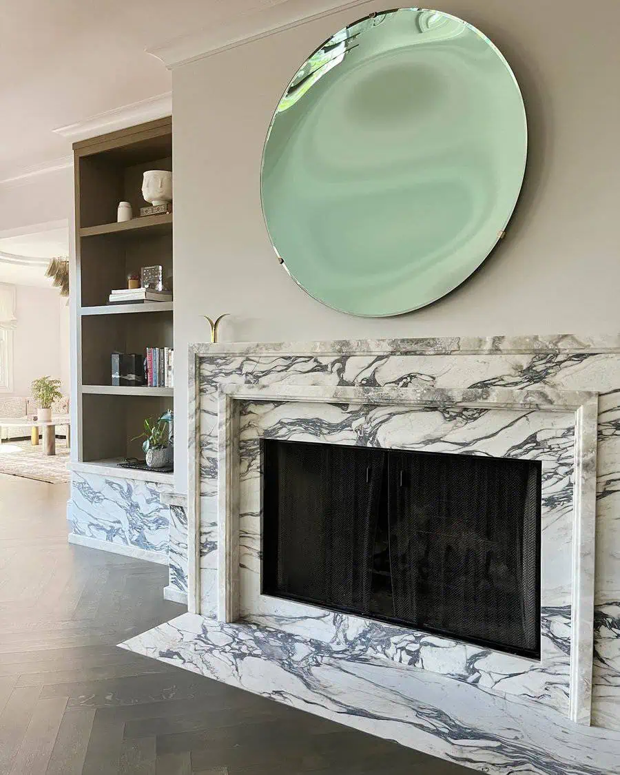 Elegant fireplace with a stunning marble surround, complemented by a large round mirror above.