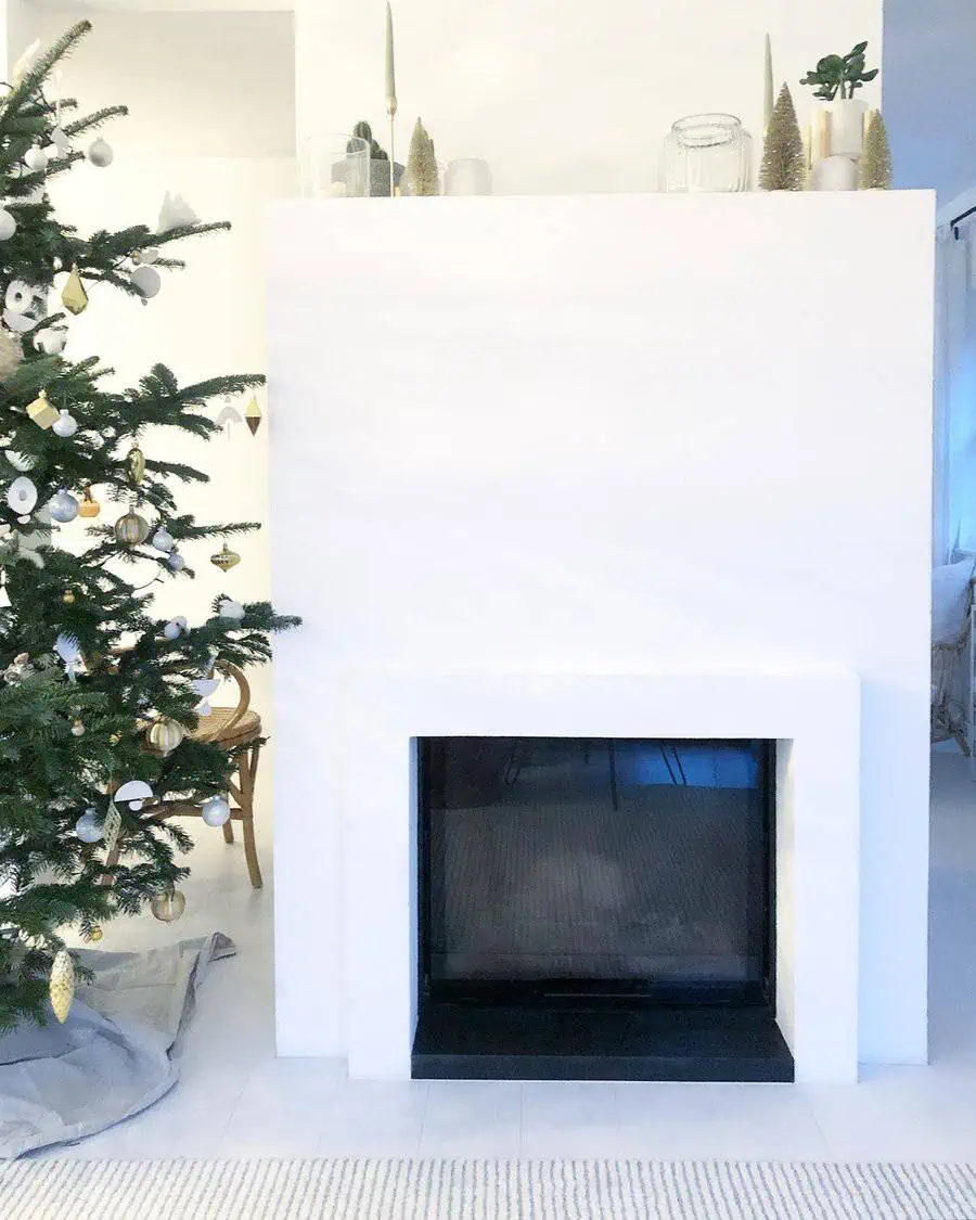 Minimalist fireplace design with a sleek white surround, complemented by festive decorations and a Christmas tree.