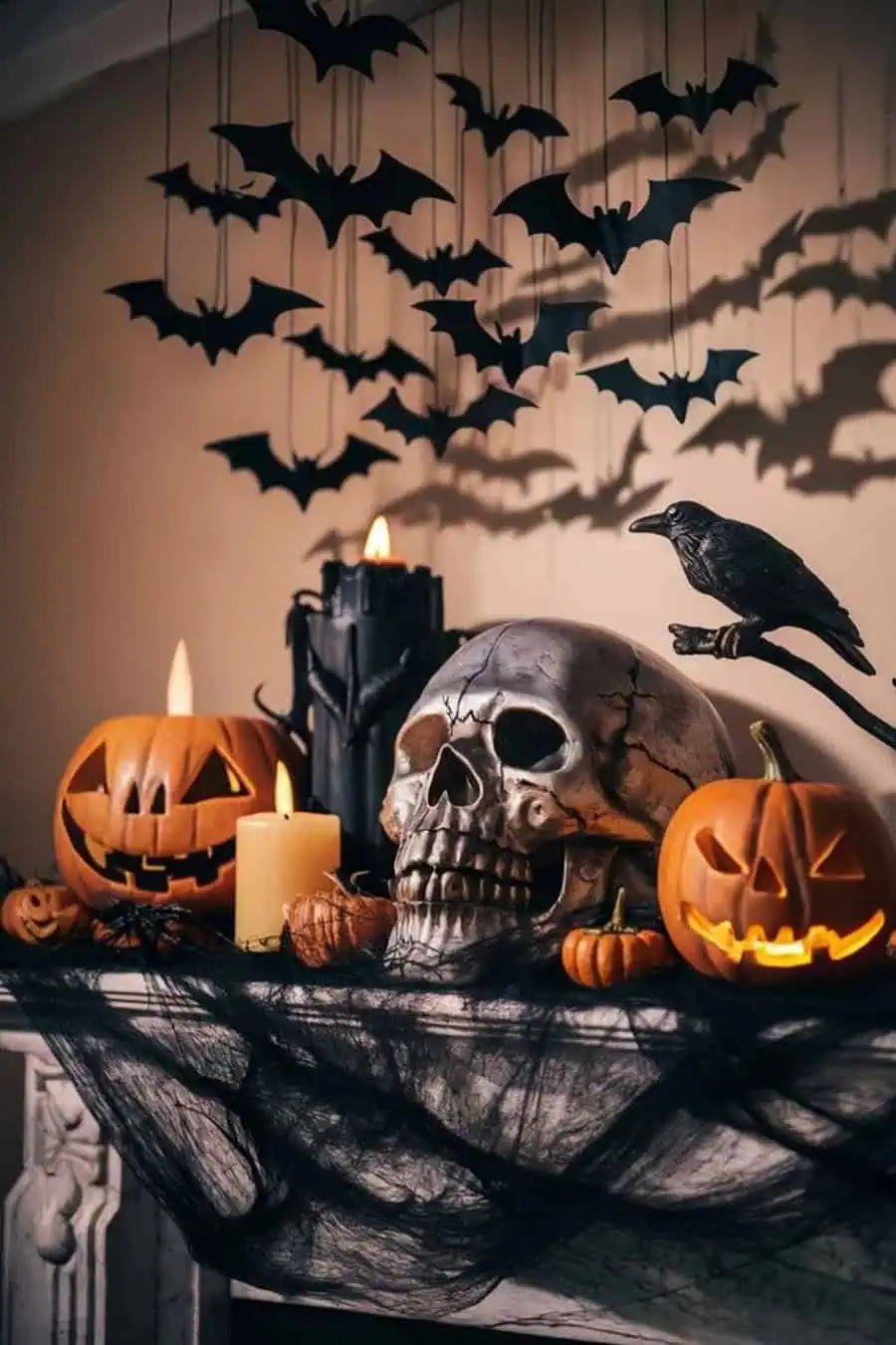 Spooky Halloween mantel decor featuring carved pumpkins, a skull, candles, and hanging bats.