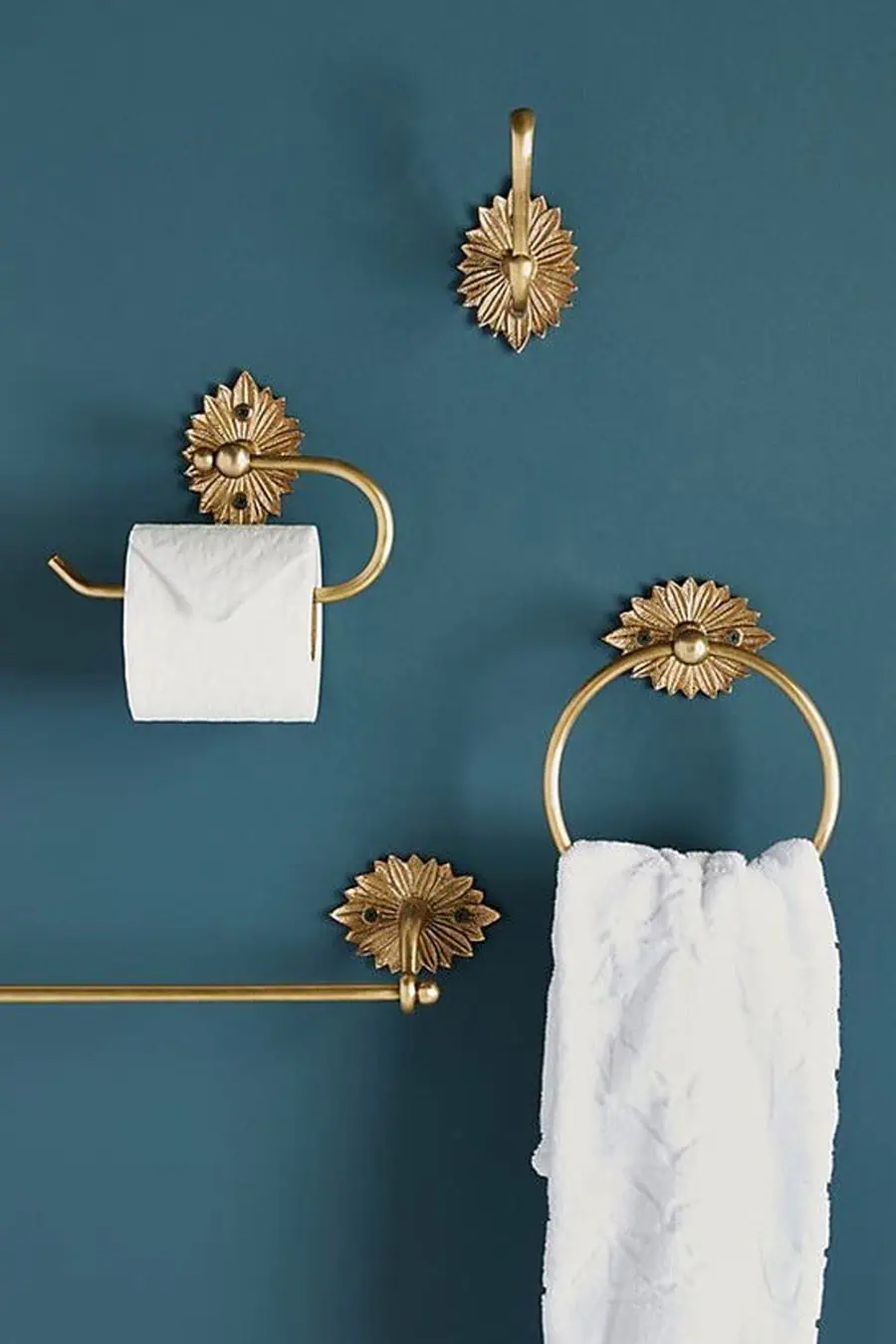 Gold Art Deco bathroom fixtures, including a towel ring, hook, and toilet paper holder, against a teal wall.