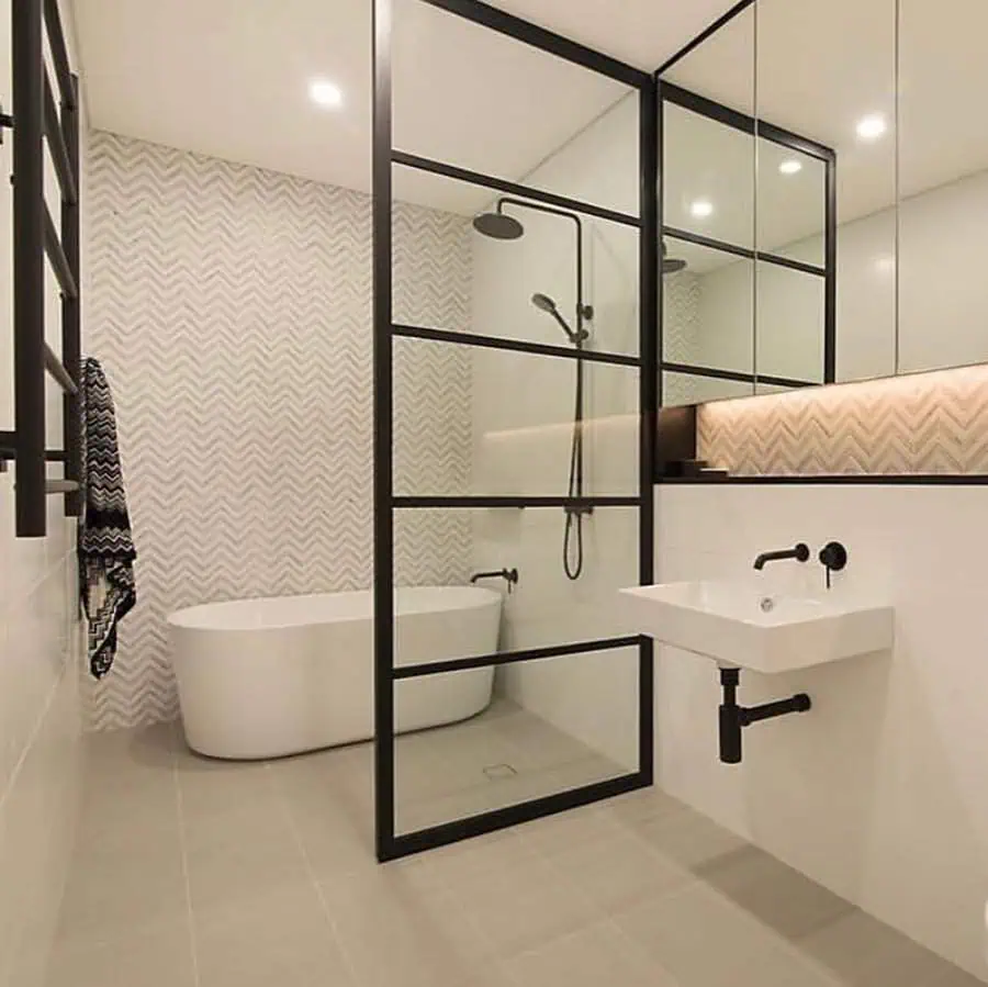 Minimalist Art Deco bathroom with black metal-framed glass panels and a freestanding bathtub.