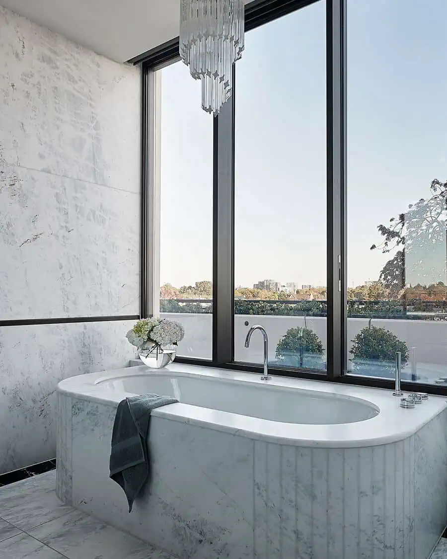 Modern Art Deco bathroom with a marble bathtub, large windows, and a crystal chandelier.