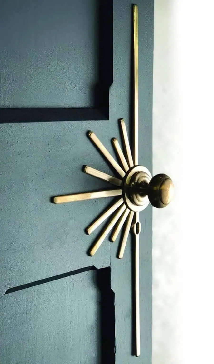 Close-up of Art Deco brass sunburst door hardware on a dark-colored door.