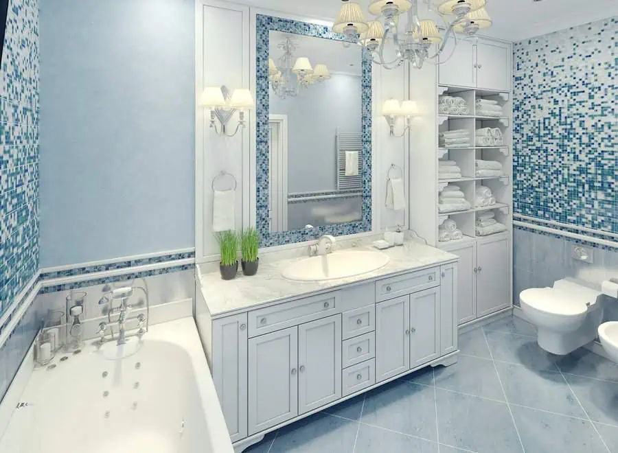 Light blue Art Deco bathroom with mosaic tile accents, chandelier lighting, and white cabinetry.