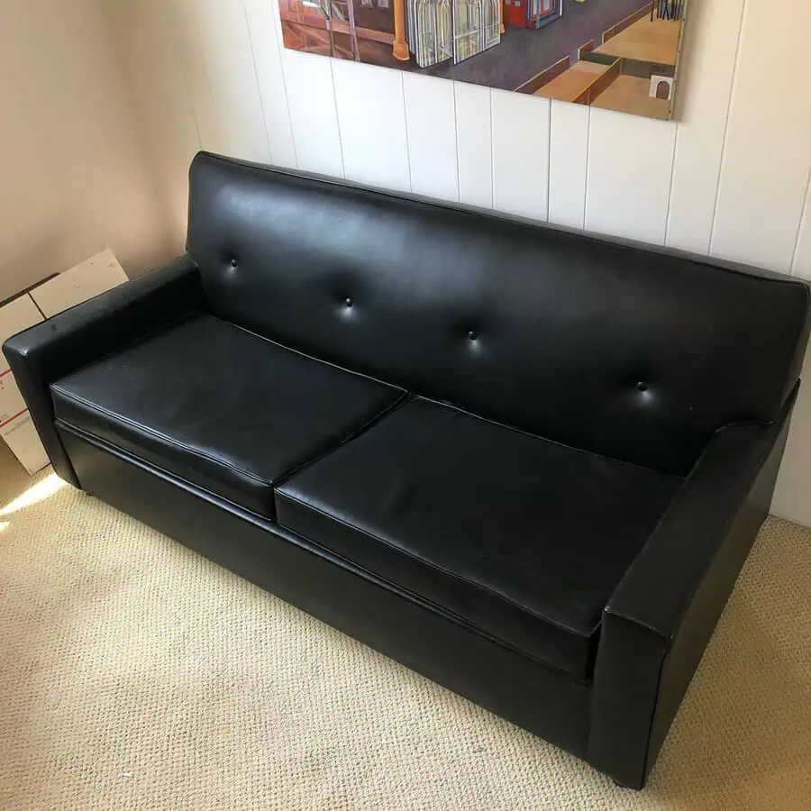 Black leather sofa in a minimalist living room with a neutral carpet and wall art.