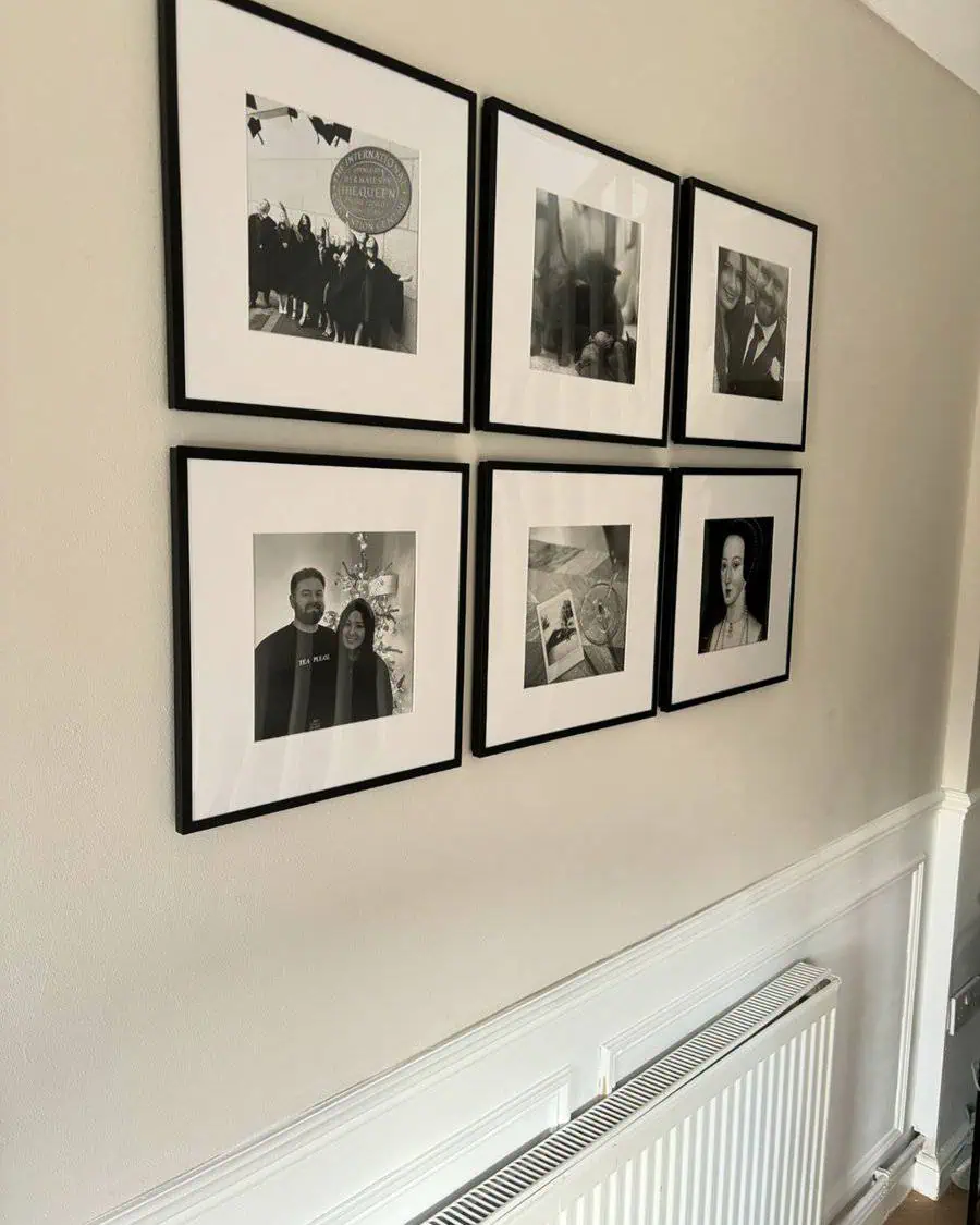 Black-and-white photo gallery wall with simple black frames in a neutral-toned hallway.