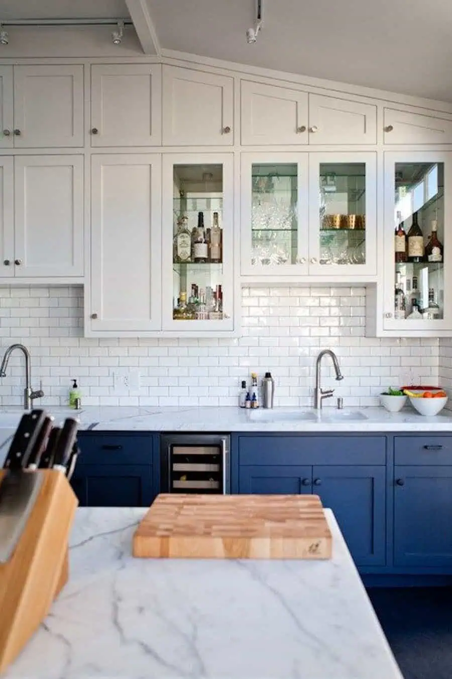 Modern kitchen with dark blue lower cabinets, marble countertops, and white upper cabinets