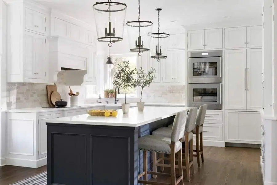 A spacious kitchen with white cabinetry, a dark island, and large pendant lights above the counter.