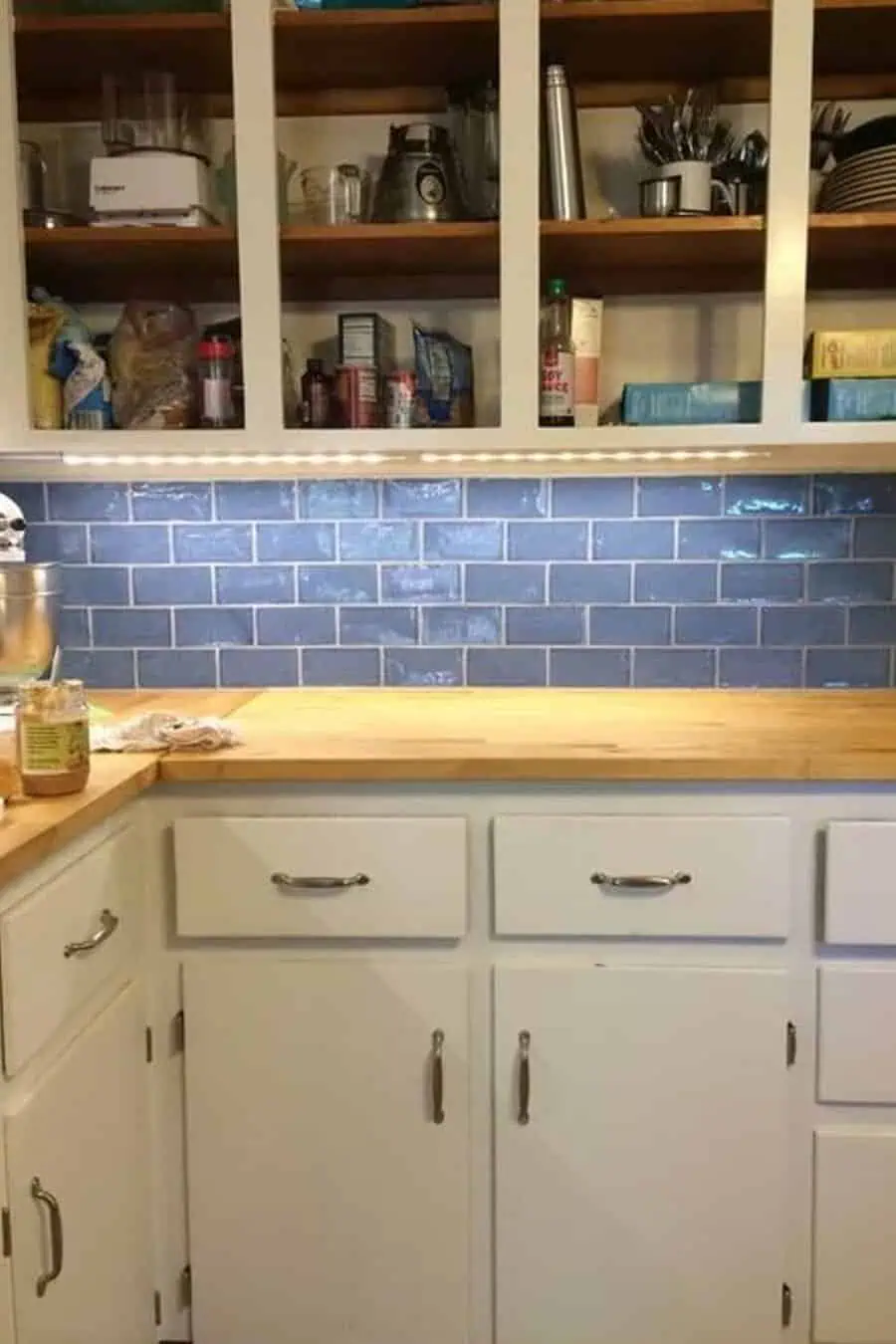 A kitchen with white cabinetry, wooden countertops, and a blue subway tile backsplash.