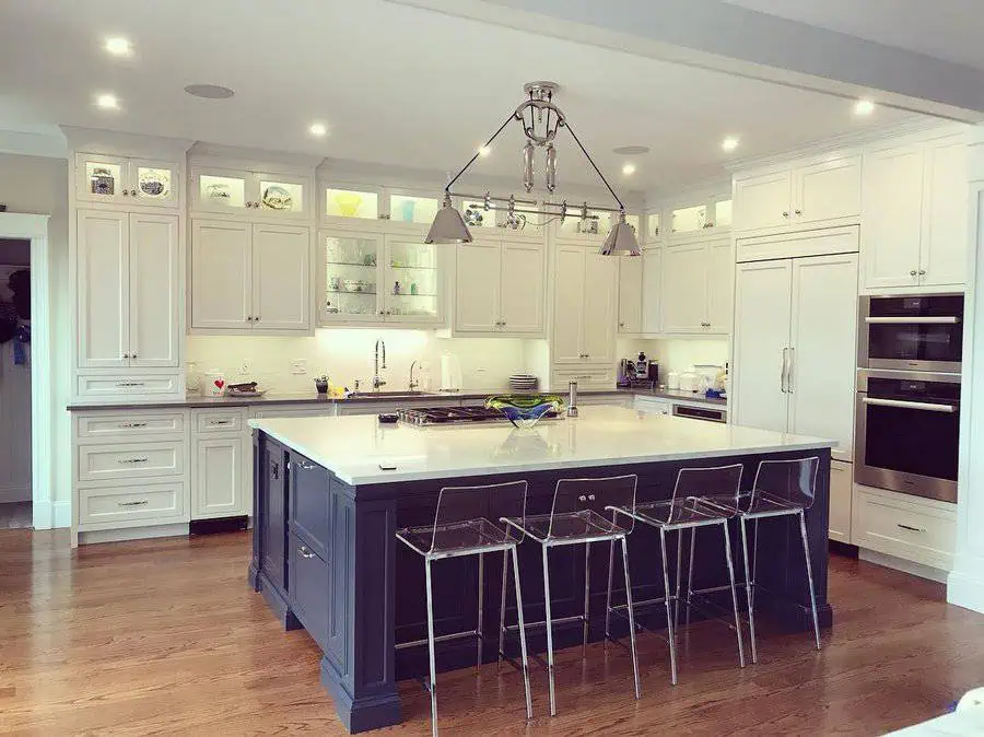 A spacious kitchen with white cabinetry, a dark island, and clear acrylic bar stools under modern lighting.