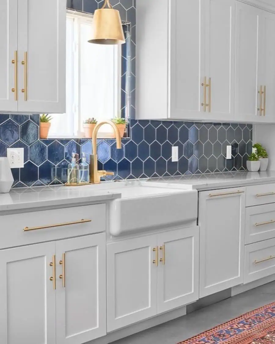 A kitchen with white cabinets, gold hardware, a blue hexagon tile backsplash, and a farmhouse sink.