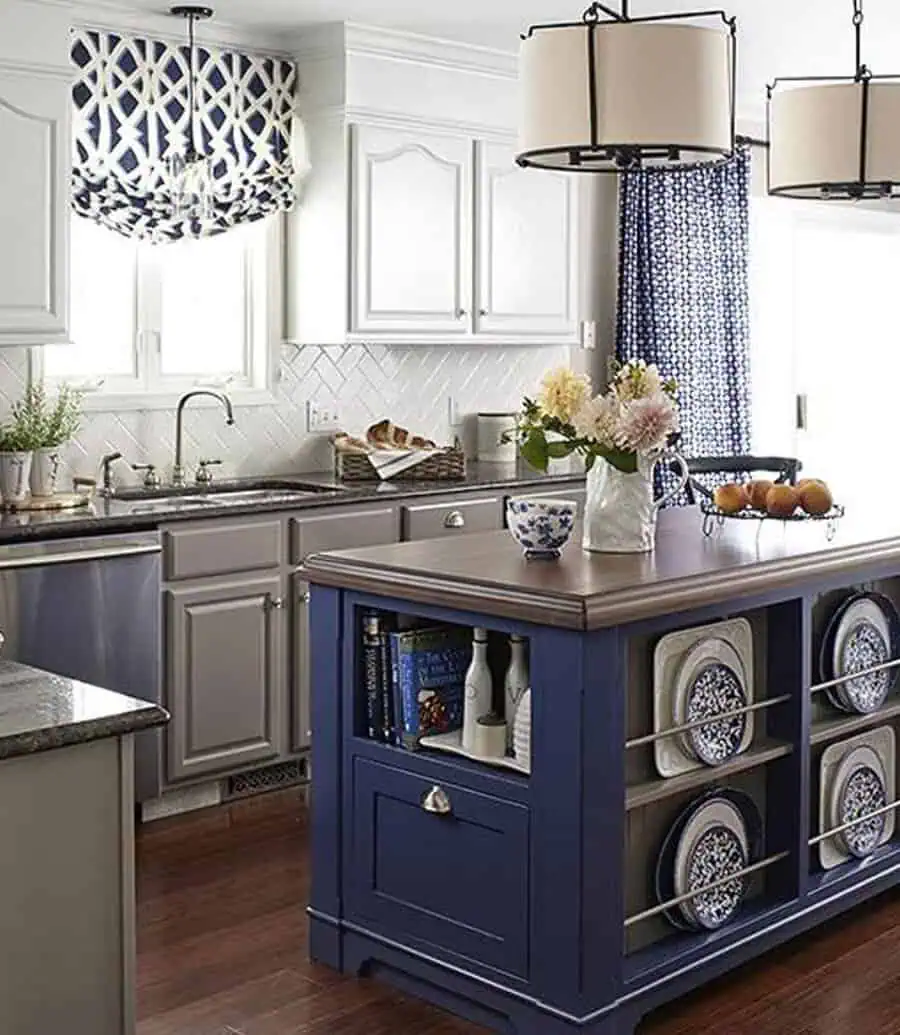 A kitchen with light gray cabinetry, a navy blue island featuring plate storage, and patterned window treatments.