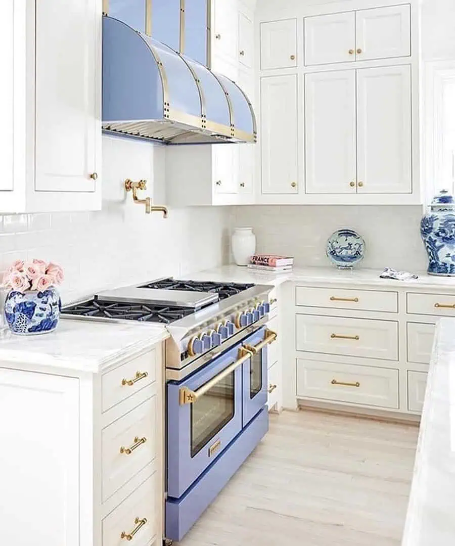 A bright kitchen with white cabinetry, gold hardware, and a striking blue and gold stove with a matching hood.