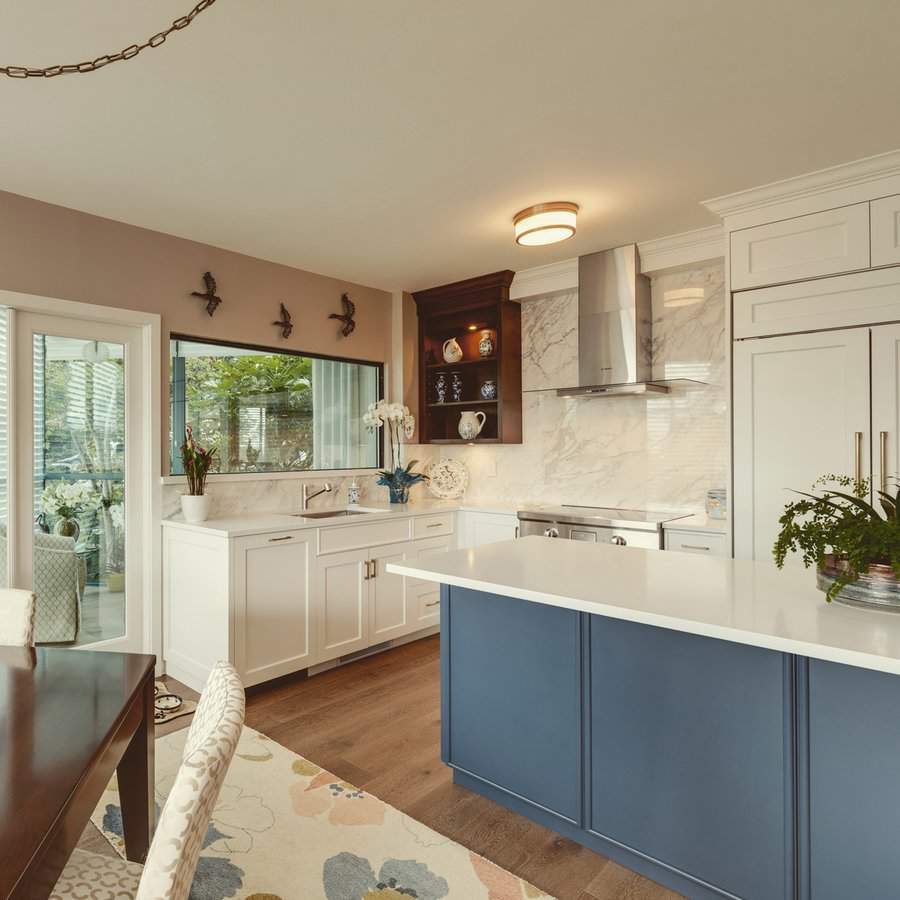 A cozy kitchen with a blue island, white cabinetry, and a marble backsplash, featuring a decorative display cabinet.