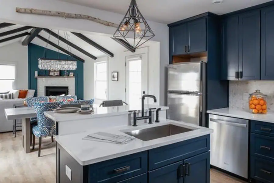 An open-concept kitchen with navy cabinets, stainless steel appliances, and a view into the living room with exposed beams and a fireplace.