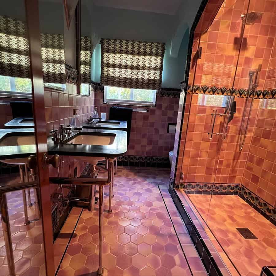 Pink and black tiled Art Deco bathroom with hexagon floor tiles, double sink, and glass shower.