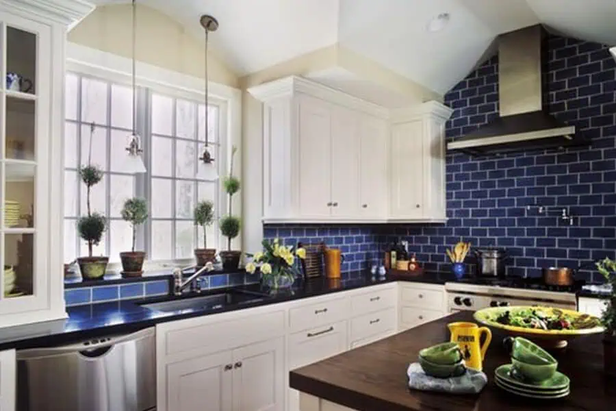 A kitchen with white cabinets, dark countertops, and blue subway tile backsplash.