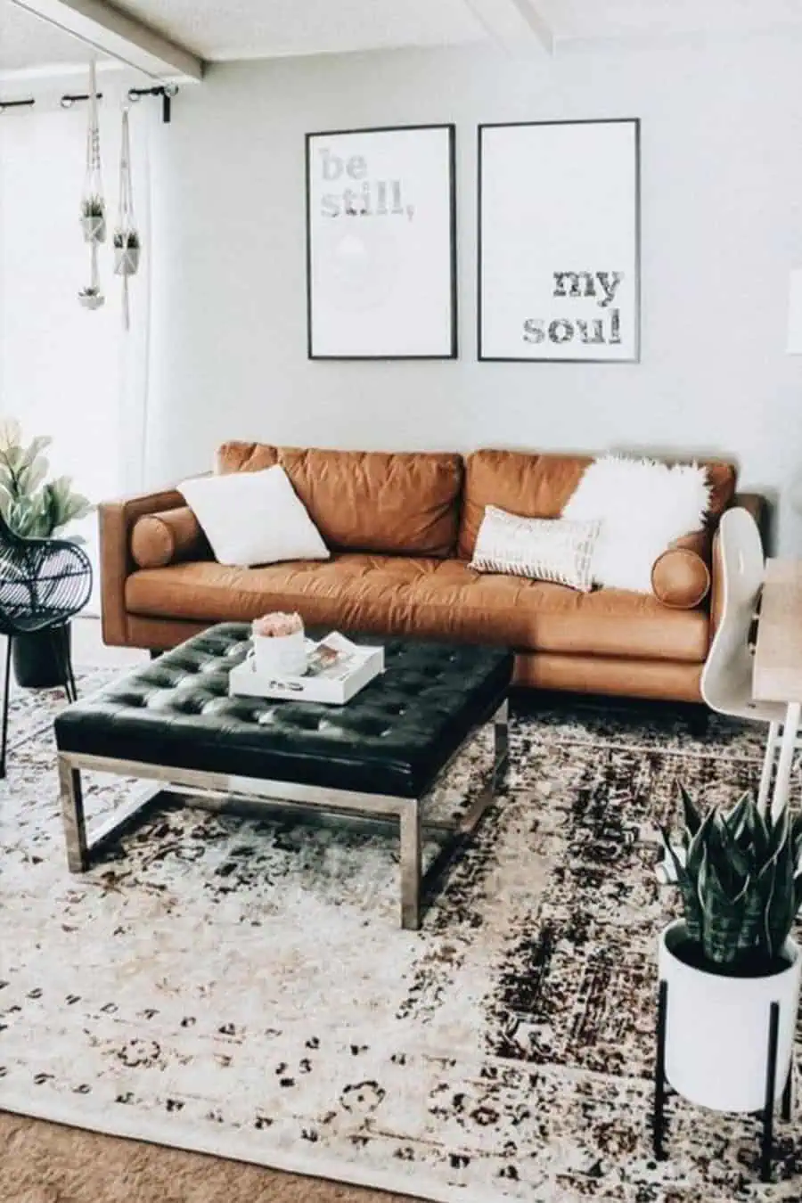 Living room with a classic tan leather couch, black tufted ottoman, and modern decor accents.