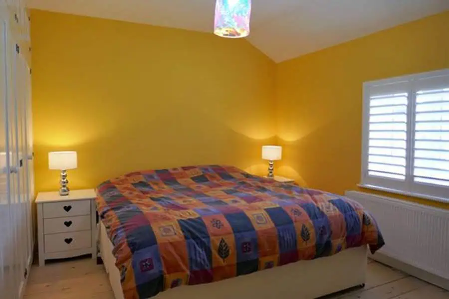 Bright bedroom with yellow walls, colorful patchwork bedding, and white bedside tables.