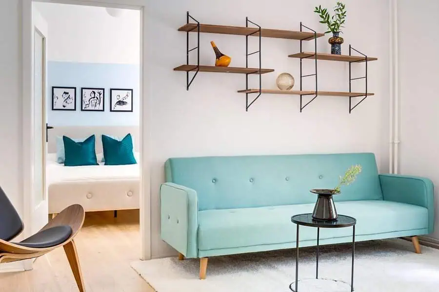 Modern living room with mint green sofa, floating wooden shelves, and a view into the bedroom.