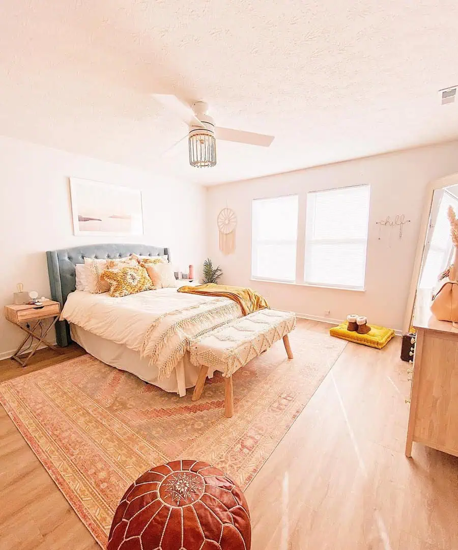 Airy bedroom with a tufted headboard, cozy textiles, and a patterned rug on wooden floors.