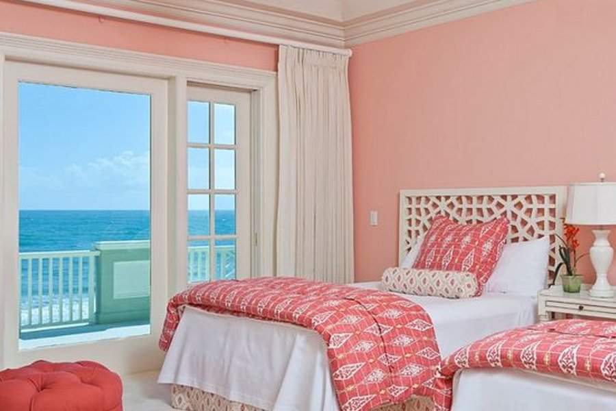 Beachfront bedroom with coral accents, twin beds, and a view of the ocean through sliding doors.