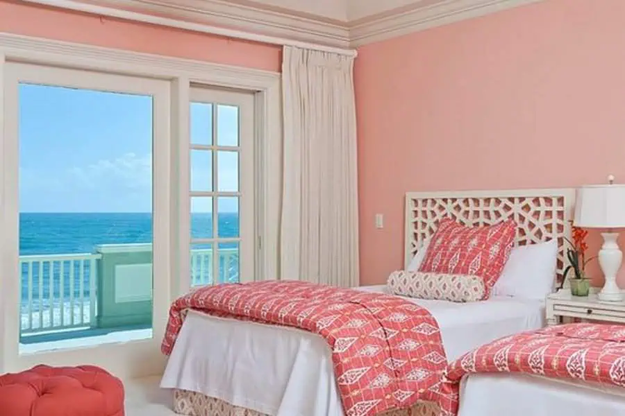 Beachfront bedroom with coral accents, twin beds, and a view of the ocean through sliding doors.