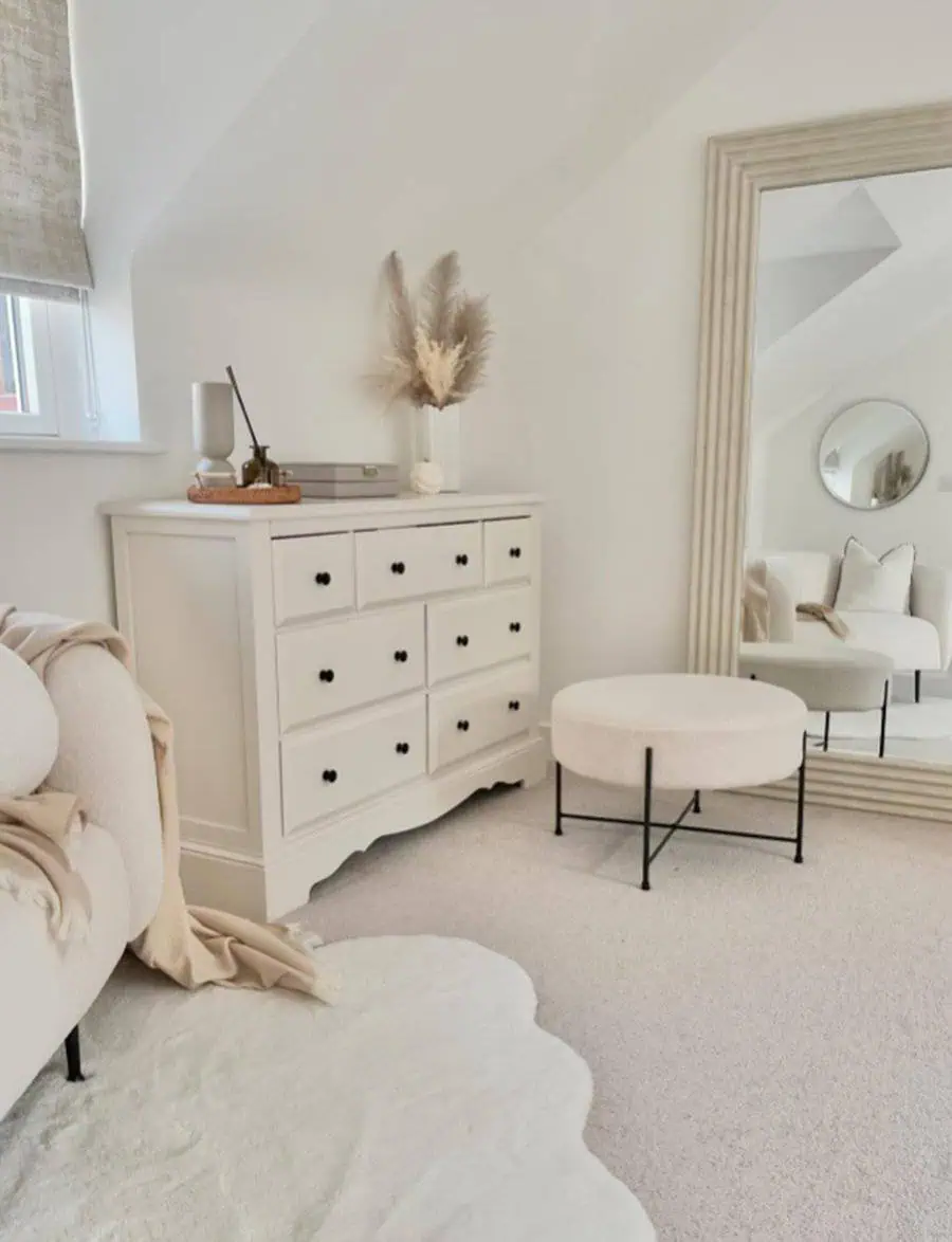 Minimalist bedroom corner with white dresser, large mirror, and soft neutral decor.