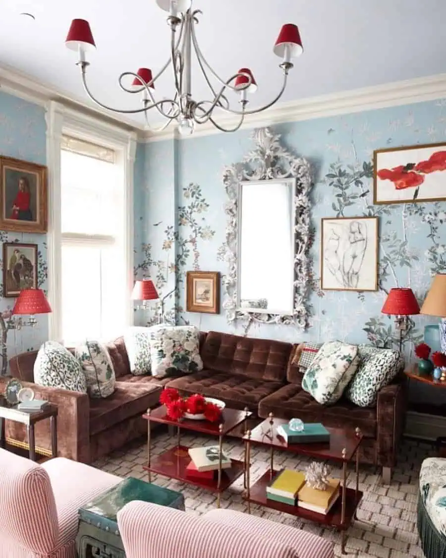 Eclectic living room with floral wallpaper, velvet sectional, and red accents in lighting.