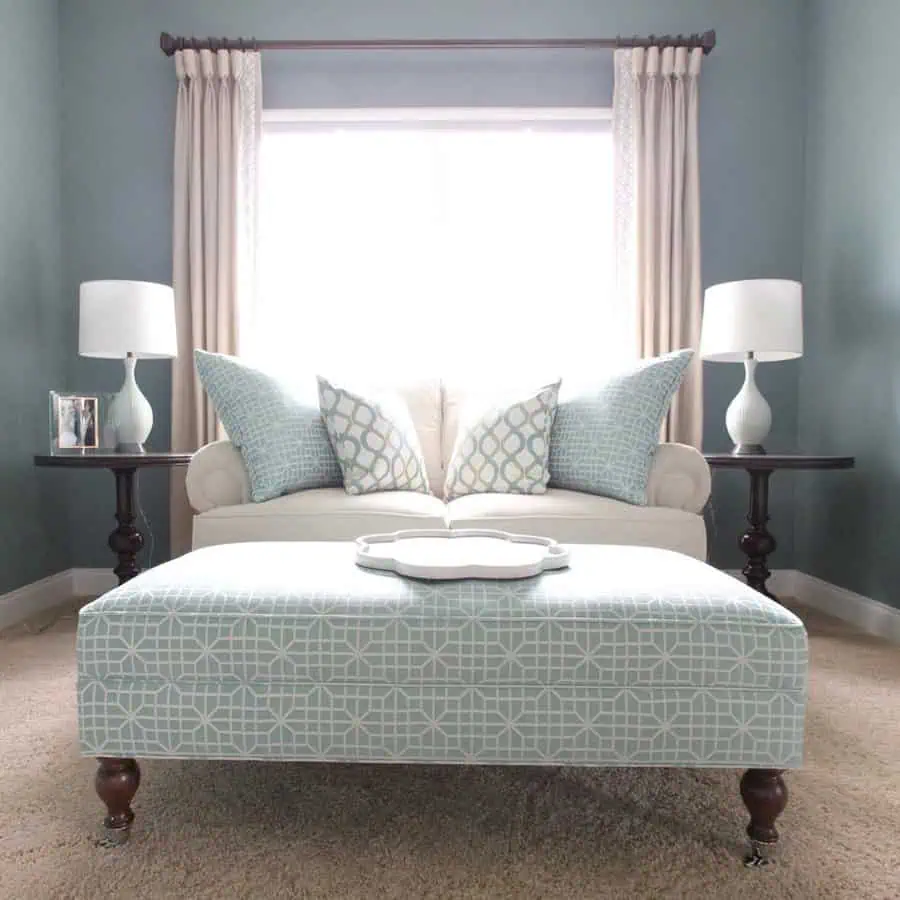 Serene living room with soft blue tones, patterned cushions, and a matching upholstered ottoman.