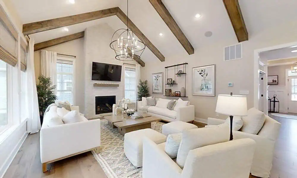 A vaulted ceiling with exposed wooden beams, light-colored furniture, and large windows create an airy, welcoming atmosphere in this spacious living room.