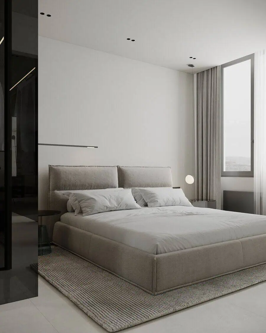 Minimalist bedroom with soft gray tones, large bed, and natural light from a floor-to-ceiling window.