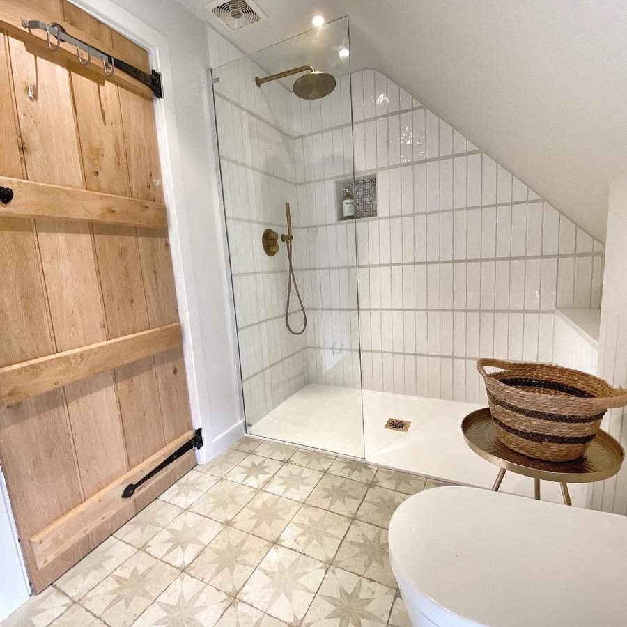 Country-style bathroom with sliding barn door, modern shower, and patterned floor tiles.