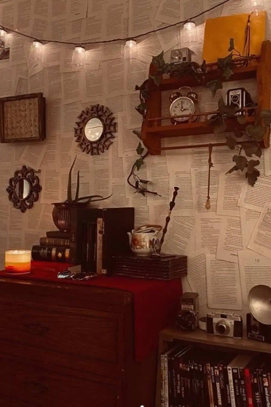 A cozy, vintage-inspired room featuring walls covered in book pages, string lights, a wooden dresser, antique clocks, mirrors, and retro cameras.