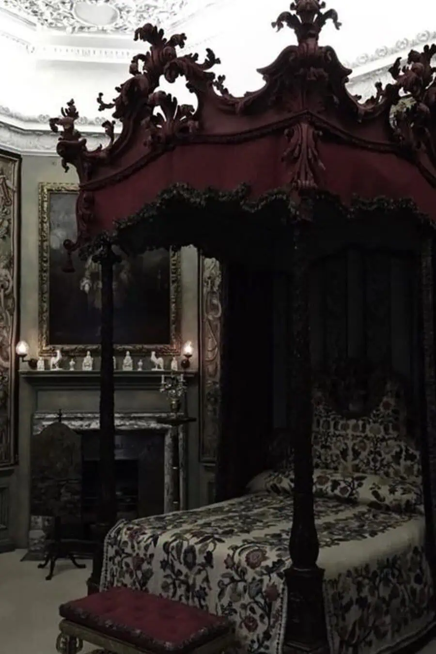 A grand four-poster bed with intricate red canopy and floral bedding, set in an opulent, dimly lit bedroom with gotic décor.