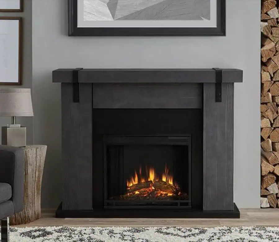 Modern electric fireplace with a sleek dark mantel, framed artwork above, and stacked wood accents.