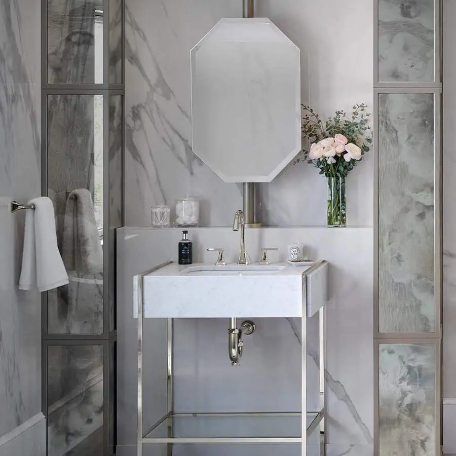 Elegant bathroom with a marble vanity, octagonal mirror, and a vase of pink flowers.