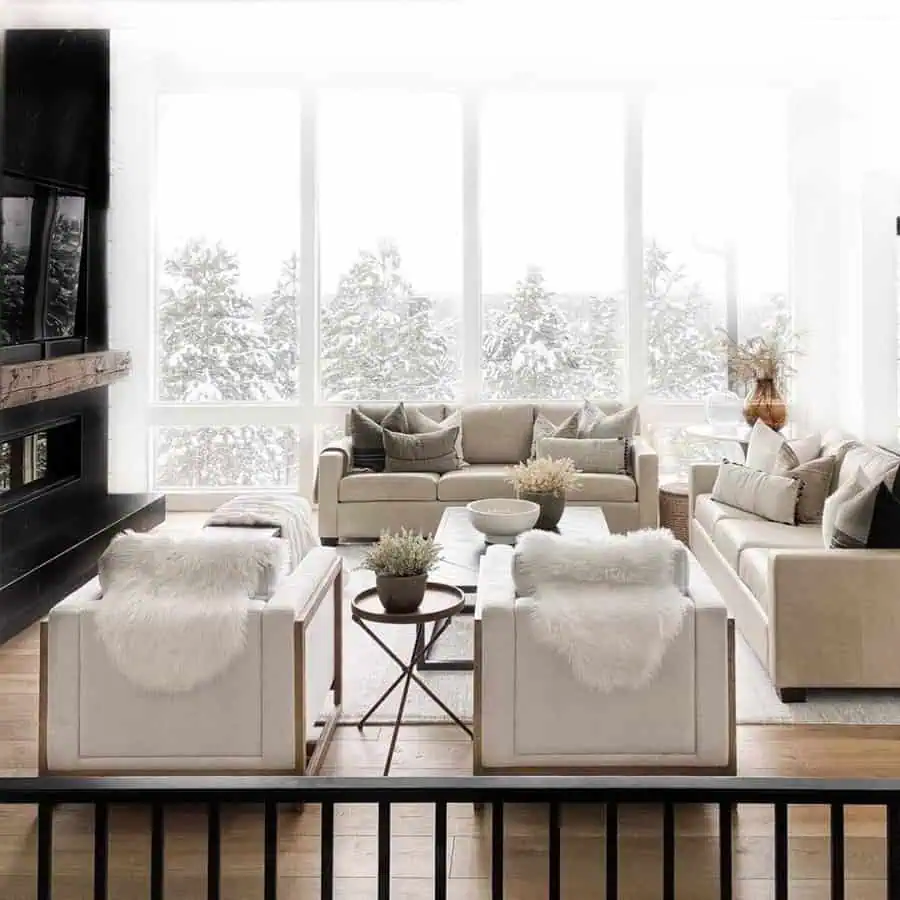 Modern living room with beige leather sofas, large windows, and snowy forest view.