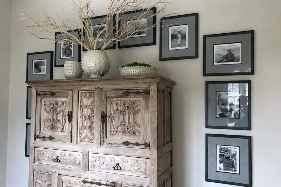 Rustic gallery wall with black-and-white family photos surrounding an antique wooden cabinet.