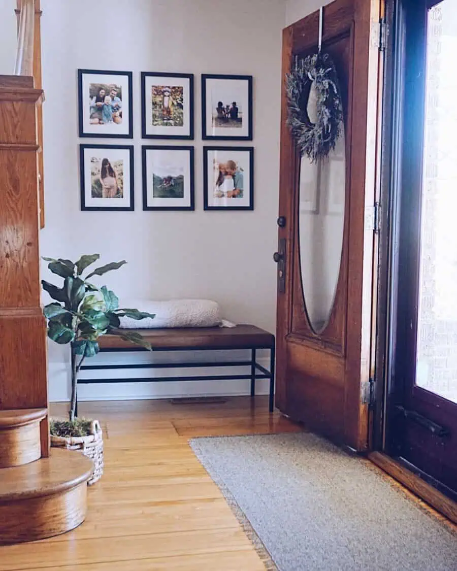 Warm entryway with family photo gallery, wooden door, bench, and a potted plant.