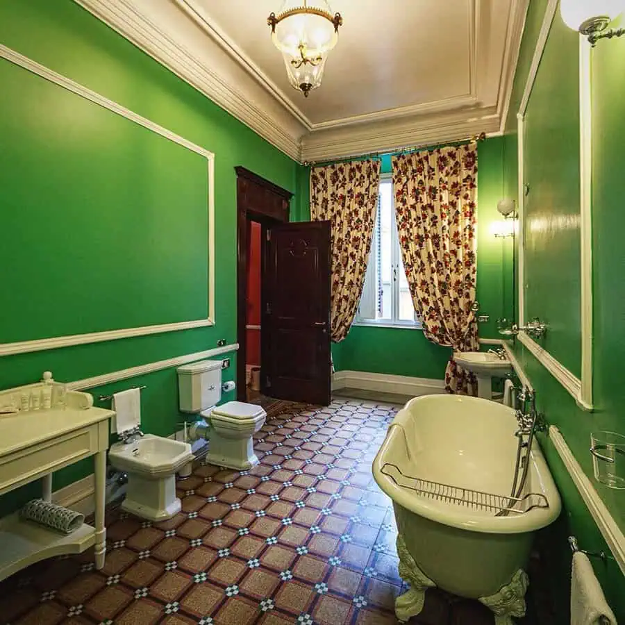 Vintage green Art Deco bathroom with freestanding clawfoot tub and floral curtains.